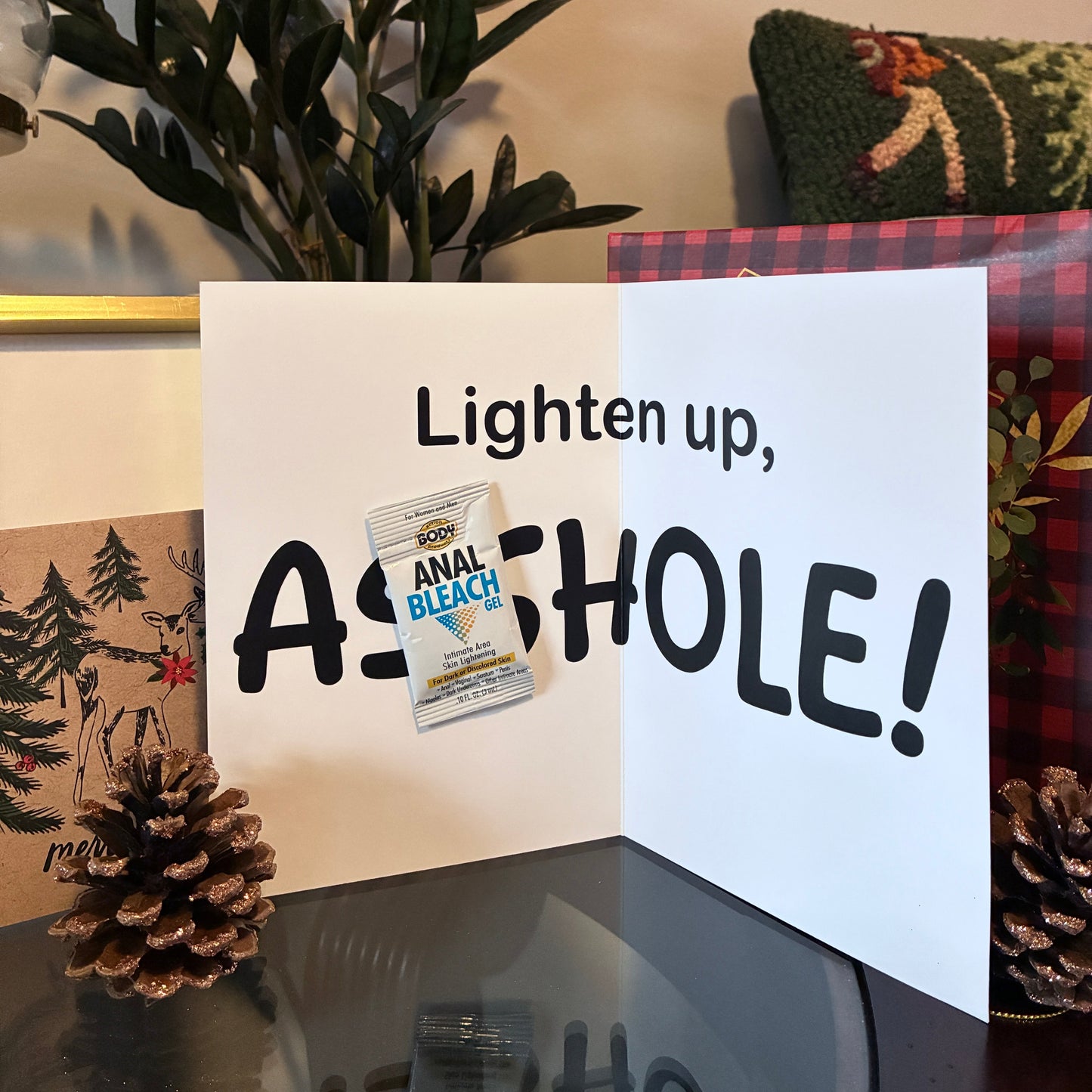 Close up of the interior of funny Christmas prank card with anal bleach packet on a table with pinecones