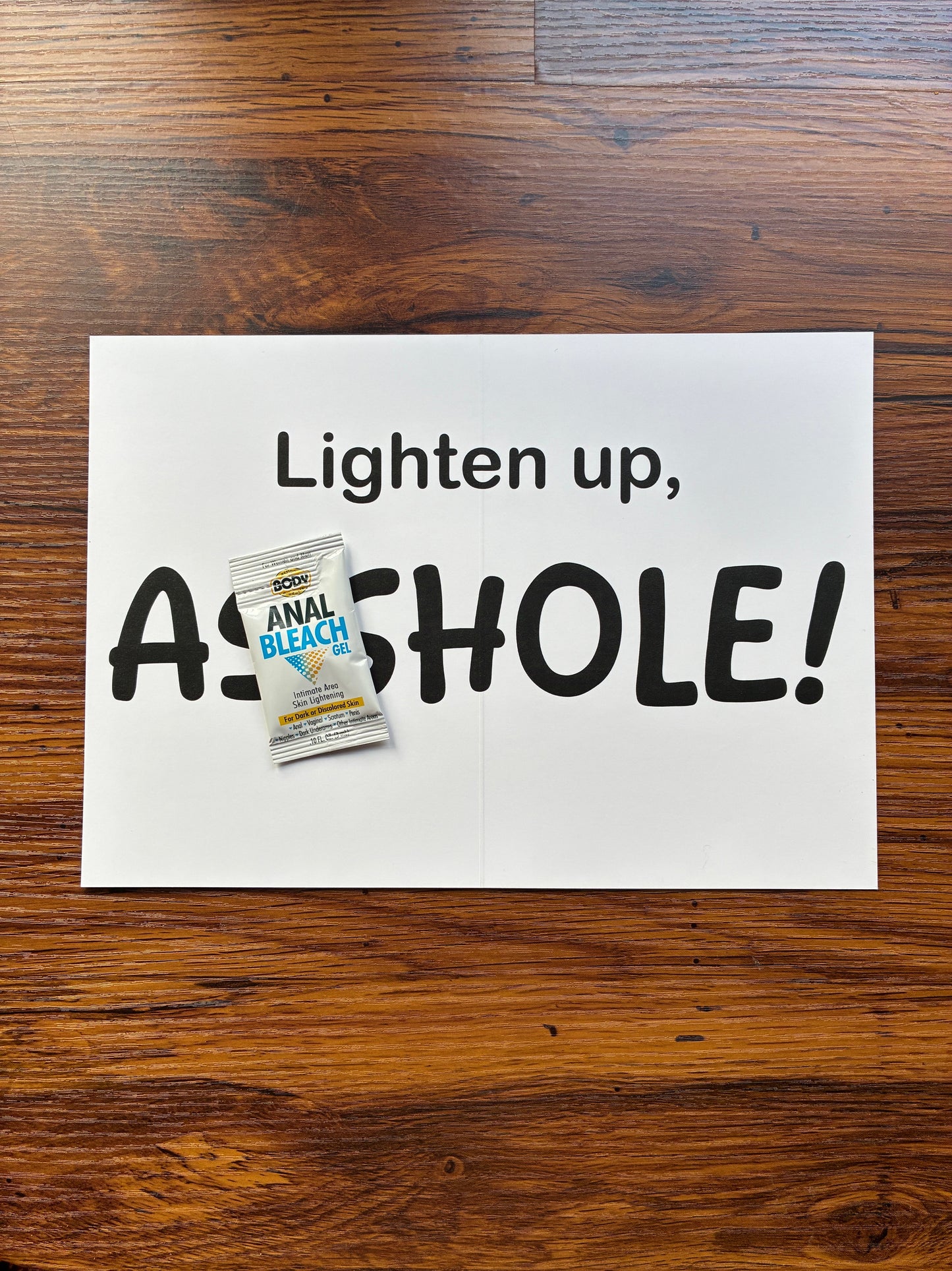 Interior of "Lighten up, Asshole!" prank gift card laid flat on a wooden desk