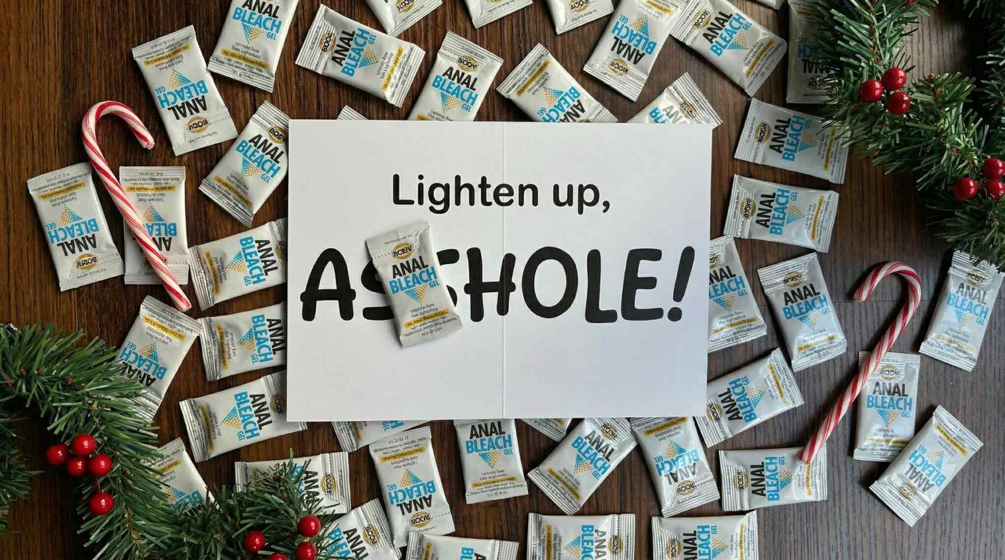 Interior of funny gag holiday card on a wooden desk surrounded by anal bleach packets, candy canes, and Christmas garland.