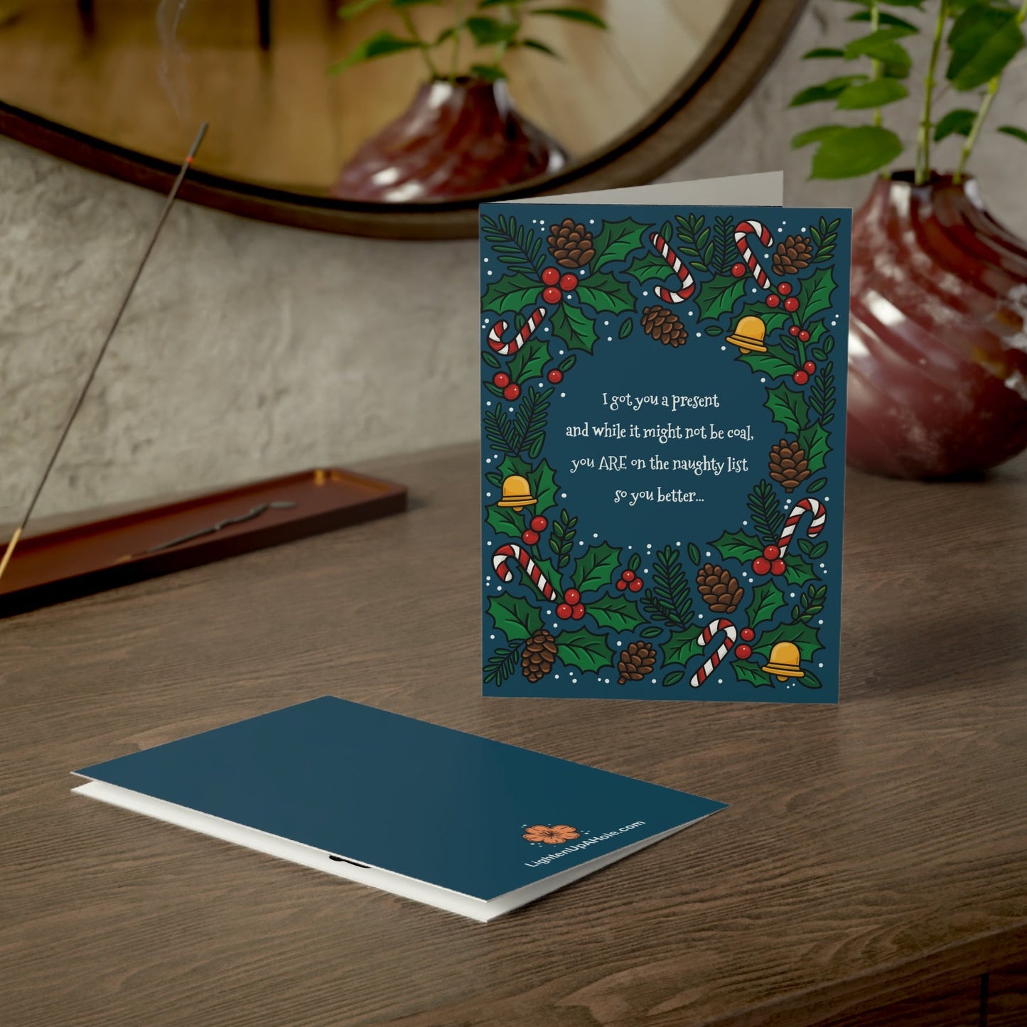 Back and front of funny prank Christmas card displayed on wooden desk.